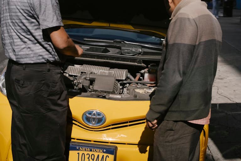 Two men examining the engine of a yellow taxi on a sunny day in New York City.